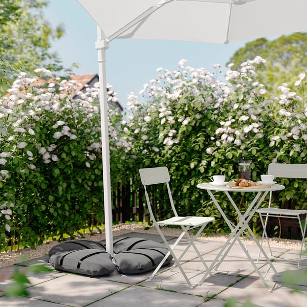 Outdoor setting with white metal table & chairs, grey cushions, white flowers, and a large white umbrella.