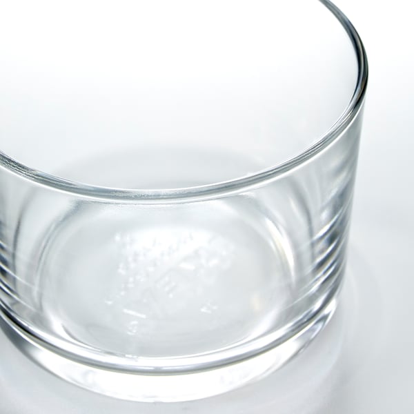 Clear, wide-mouthed glass on a white surface, reflecting light, showcasing its transparent and sturdy design.