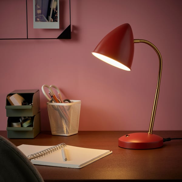 Red ISNÅLEN lamp with flexible neck on desk, lit.