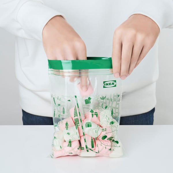 A person holding an open, transparent IKEA ISTAD bag with a green seal, showcasing its re-sealable feature.
