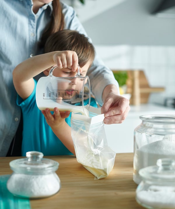 A person pours liquid into a transparent ISTAD bag on a table with jars.