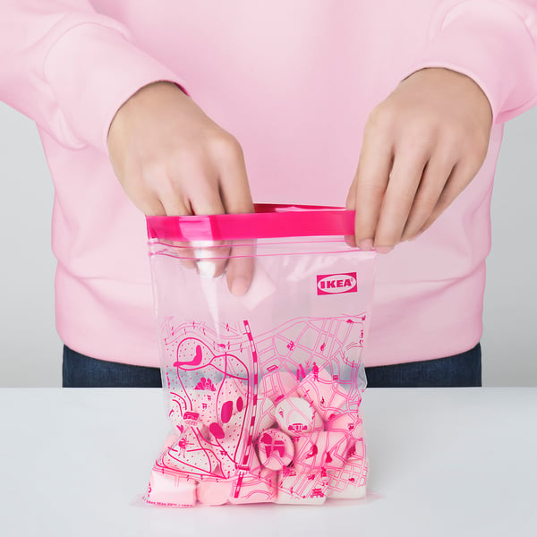 Person holds reusable IKEA storage bag, closing zip. Bag a colourful, patterned design.