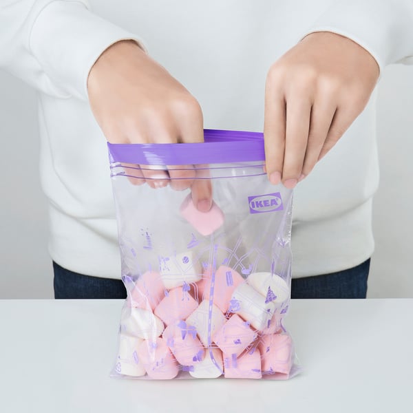 Person holding a sealed IKEA ISTAD freezer bag filled with pink and white items, demonstrating its ability to keep contents fresh and organised.