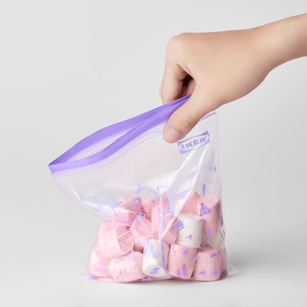 A hand holding an open purple-sealed IKEA ISTAD bag filled with pink and white items.