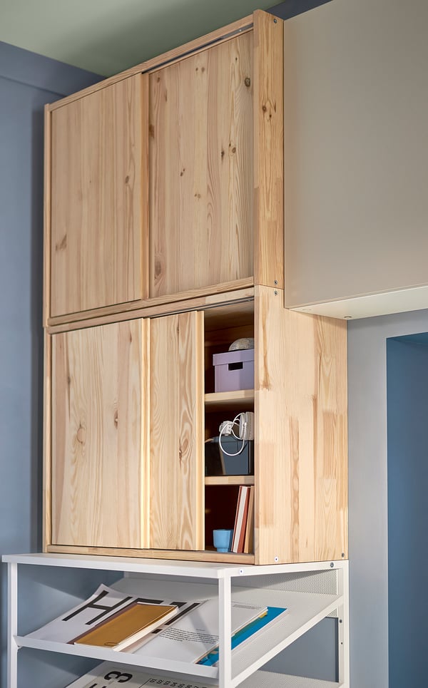 IVARs pine storage unit with sliding door, holding various items.