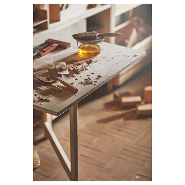Woodworking workspace with tools and oil on pine table, sawdust scattered, against tiled floor and cabinets.