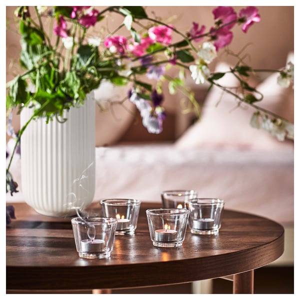 A cosy scene with lit tea candles on a wooden table next to a vase of pink and purple flowers.