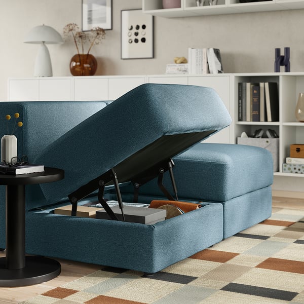 Blue sofa with storage compartment open, showing books and blankets inside.
