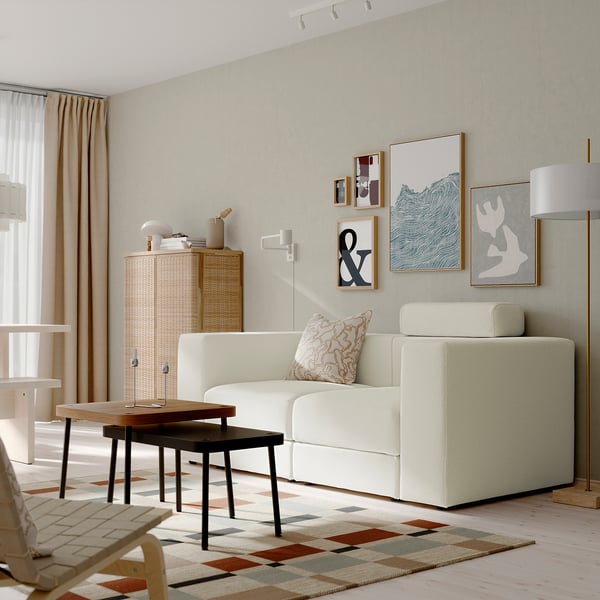 Minimalist living room with JÄTTEBO white modular sofa, geometric rug, wooden coffee table, and wall art. Sofa is large compared to table and rug.