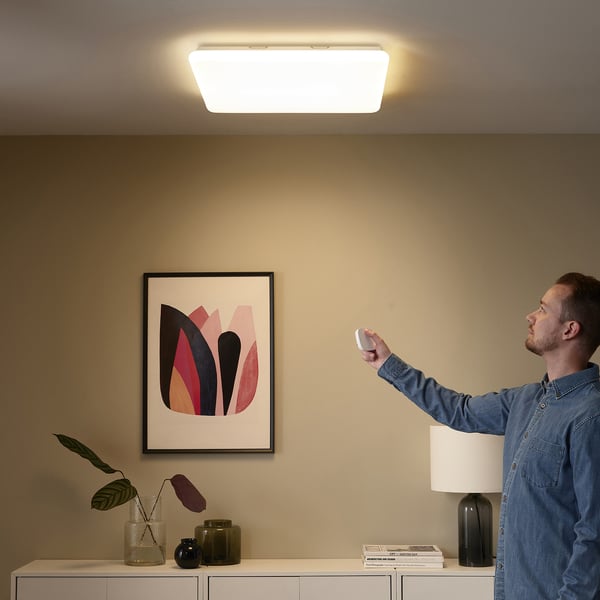 Person with remote controlling ceiling smart light panel. Art and decor on wall.