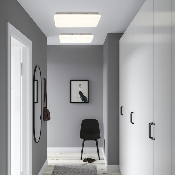 Modern hallway with grey walls, white led panel, black chair, and round mirror.