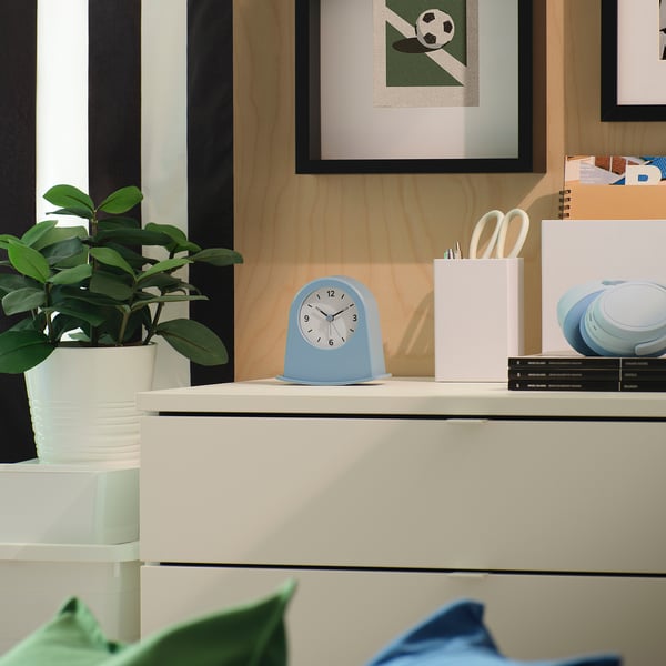 Desk with KÄRRSÅNGARE clock, white organiser, scissors, green plant, football picture.