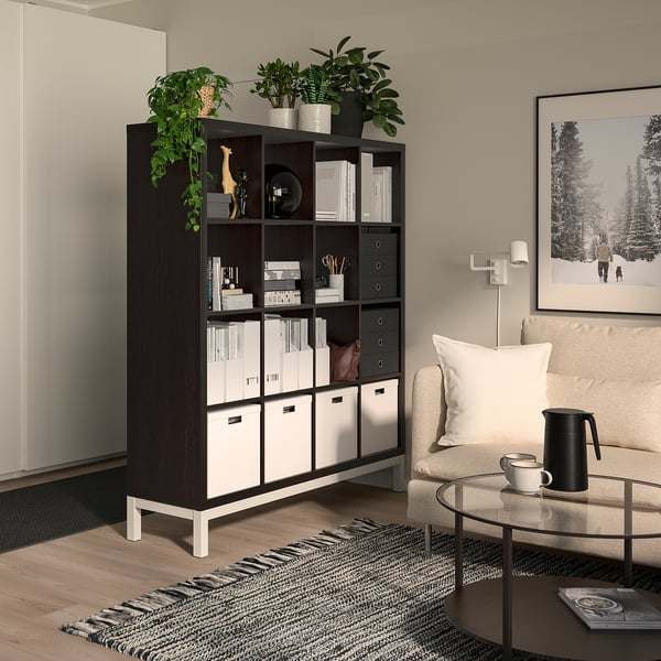 Living room with KALLAX divider, plants, decor. Armchair, coffee table, rug, art.