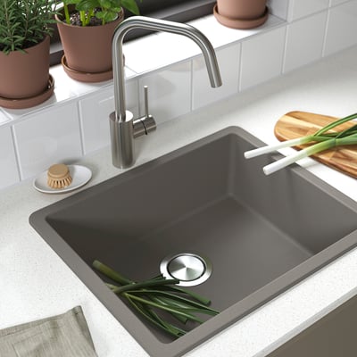 Dark kitchen sink with stainless tap, green onions, and potted herbs on a white countertop.