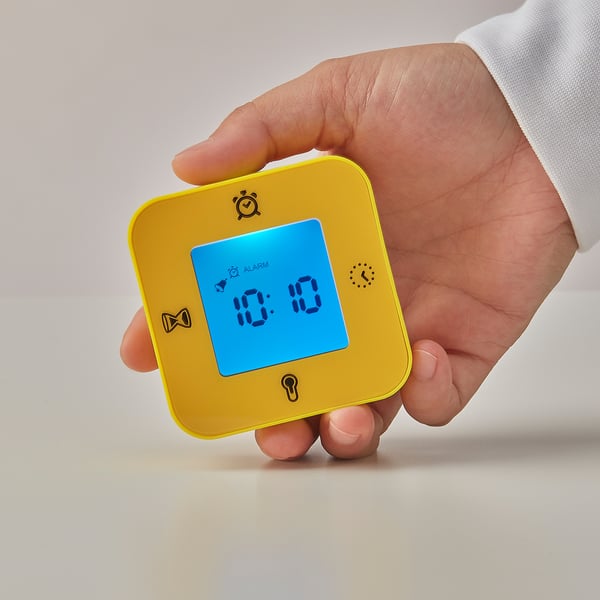 A hand holds a bright yellow ikea KLOCKIS clock, displaying the time 10:10 on its clear blue screen, showcasing its time function.