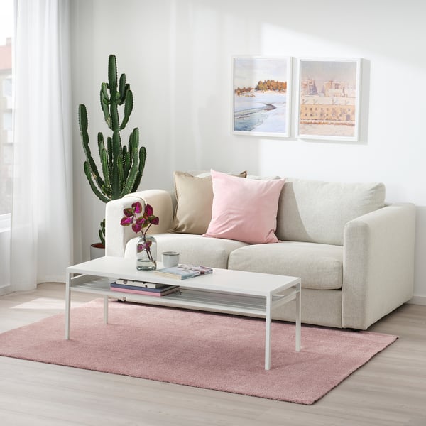 Modern living room with beige sofa, cactus, white coffee table, & KNARDRUP rug in pale pink.