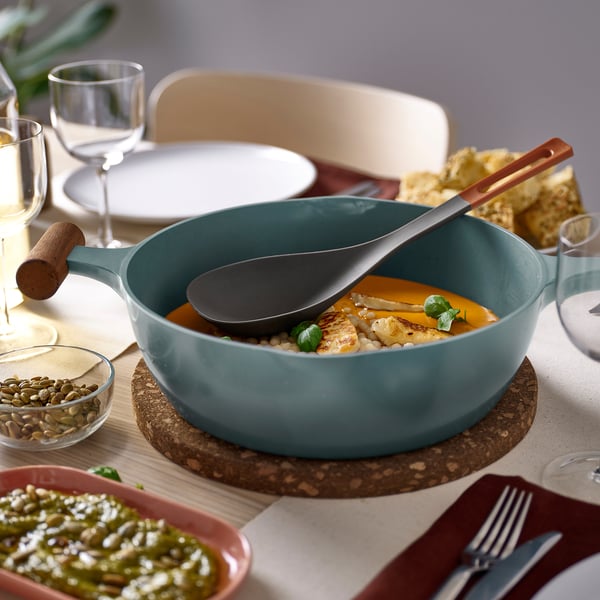 Modern blue KNORRHANE deep spoon rests in pan, larger than adjacent dishes and glassware, fits comfortably in hand for serving.