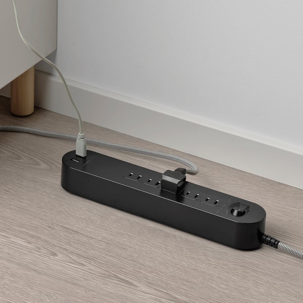 Black multi-socket with usb ports on wooden floor, granting power to devices.