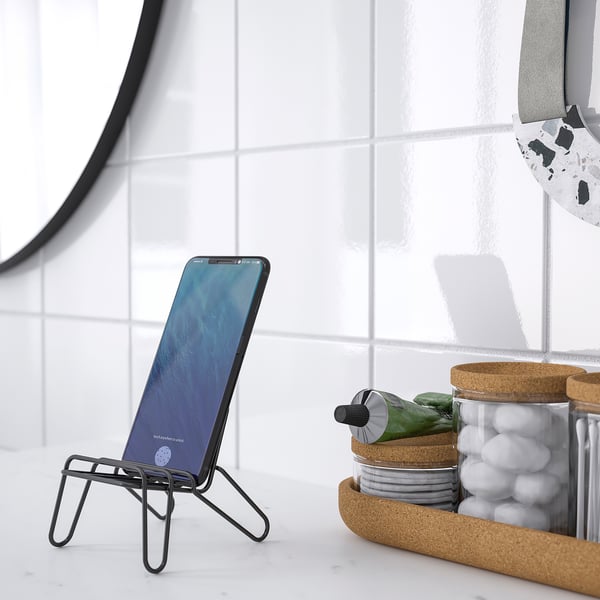 Metal phone stand in bathroom with cotton swabs, marbles, and mirror.