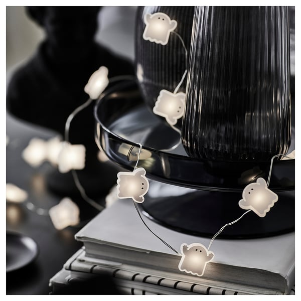 String of ghost-shaped halloween lights draped over decorative items, emitting a warm glow.