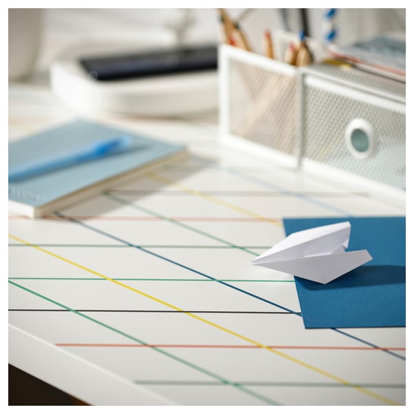 Colourful desk with paper plane, books, and stationery. White plane on blue book, multicoloured lines on white surface.