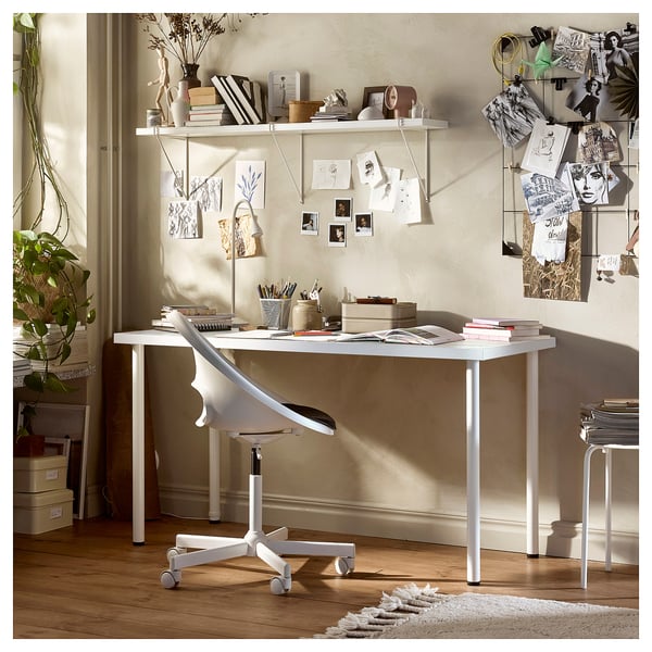 Modern office space with white lagkpten desk, ergonomic chair, and decorated shelves. Neutral tones, natural light, and artistic wall display.