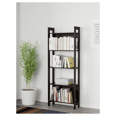 Black wooden bookshelf against a white wall, holding various books and magazines on four shelves. Beside it, a large potted green plant.