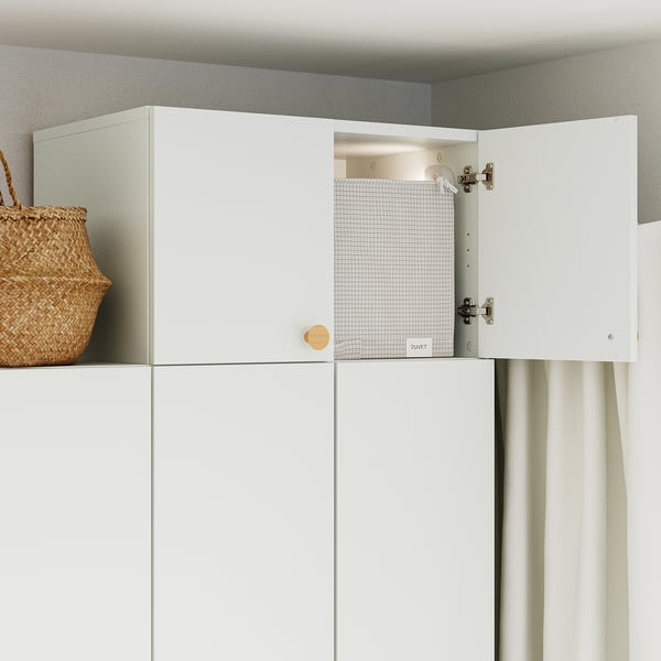 White cabinet with one door open, revealing inside. On top, a wicker basket is placed.