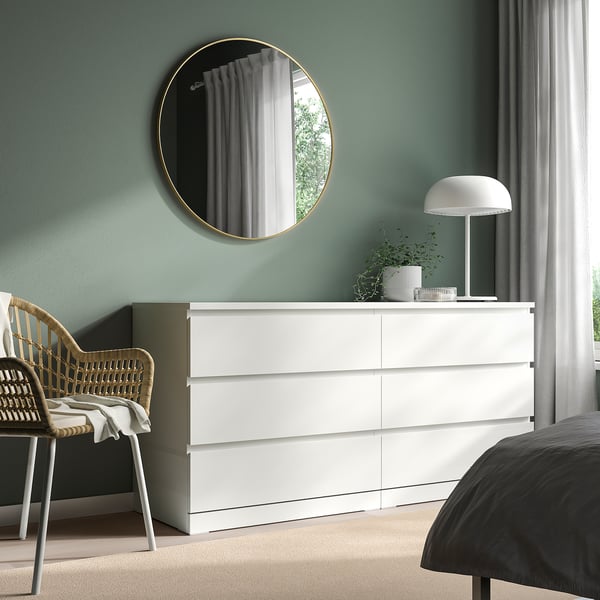 Modern bedroom: gold mirror, white dresser, plant, grey bed.