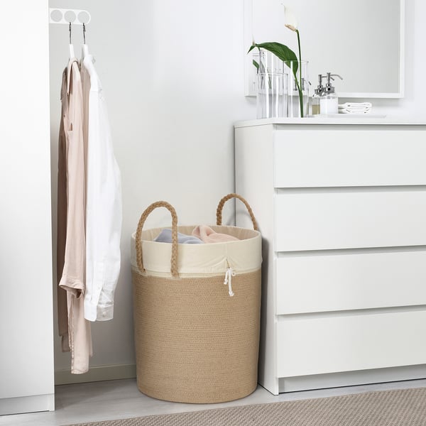 Beige LJUNGAN laundry basket with rope handles, holding pink/blue clothes, beside white dresser.