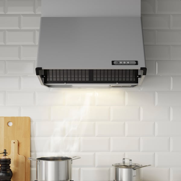 Modern kitchen hood with control panel and led light, mounted on white brick wall. Two pots below, wooden utensils to the side.