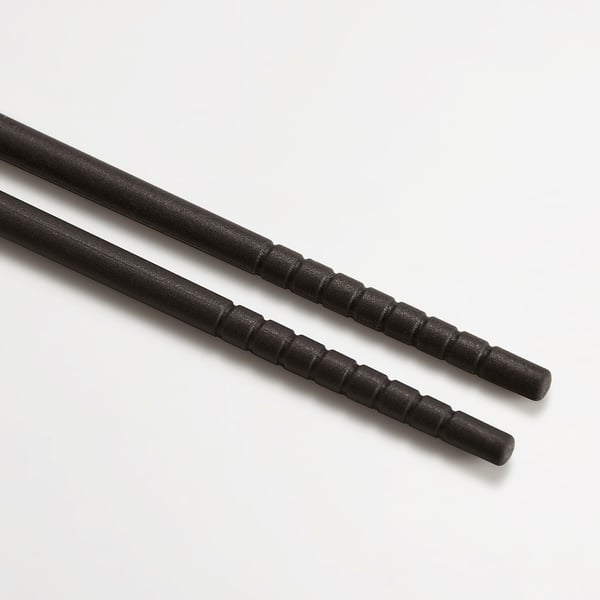 Black silicone chopsticks with grooved texture, laid diagonally on a light surface.