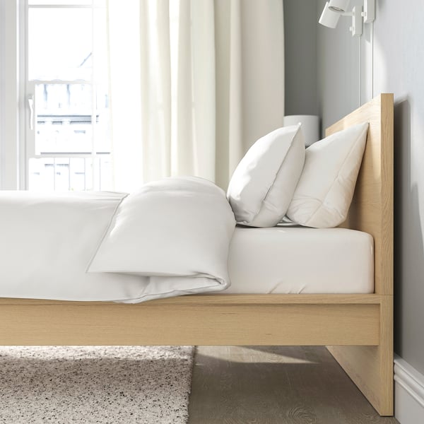 White bed with wooden frame and pillows in clean room. High headboard, slatted base.