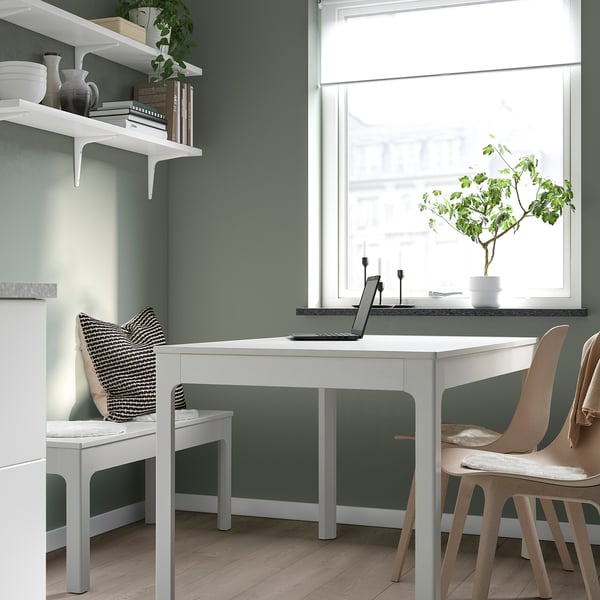 Home office with green walls, dual desks, plants, & natural light.