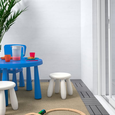 Kids play area with blue table, stools, & cups. Gray-tan rug.