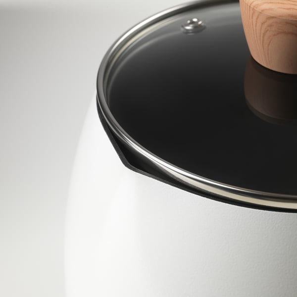 Black saucepan with glass lid and wooden handle on white surface.
