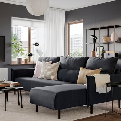 Contemporary dark grey MANNARP sofa with chaise, colourful cushions, in bright room with plants.