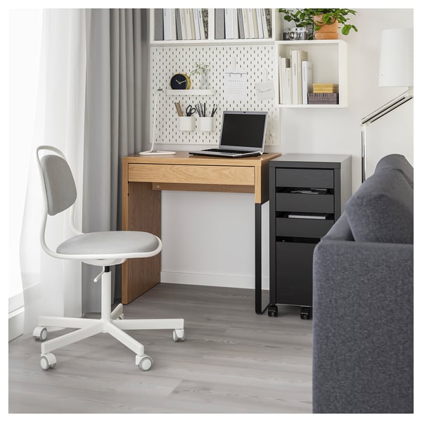 Modern home office with MICKE desk, swivel chair, laptop, and shelves with books and plants.