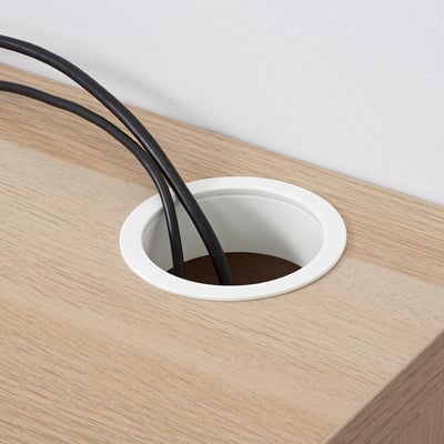 A wooden desk with a circular cable management port, housing black cables.
