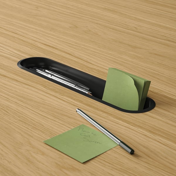 Black table tray holding pens and green sticky notes, one with handwritten text, on a wooden table.