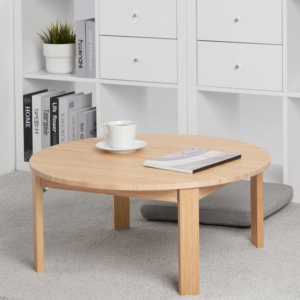 Bamboo coffee table with foldable legs, cup, and magazine. Near white shelf with books and plant.