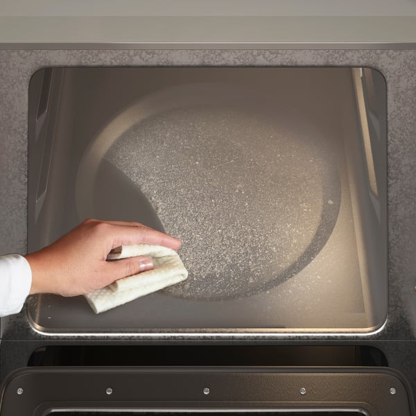 Hand wiping oven glass with cloth inside stainless steel oven, showcasing easy cleaning functionality.