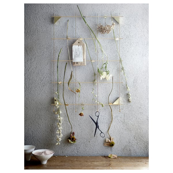 Gold-colored grid wall organiser with hanging dried flowers, scissors, and bowls; modern, minimalist design.