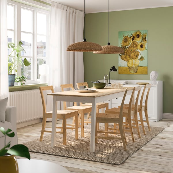Cosy dining room with wooden table, chairs, and pendant lamp. Sunflowers, curtains, and plants enhance warmth and natural light.