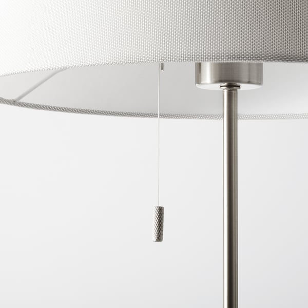 Modern, silver NYFORS floor lamp with adjustable height, showcasing sleek design and sturdy base. A white textile shade and metallic accents.