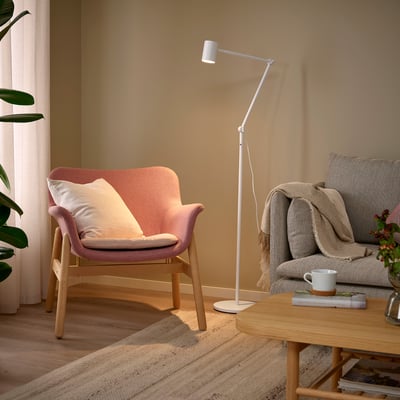 Stylish NYMÅNE white floor lamp casts adjustable light, fitting perfectly between cosy chairs in modern living space.