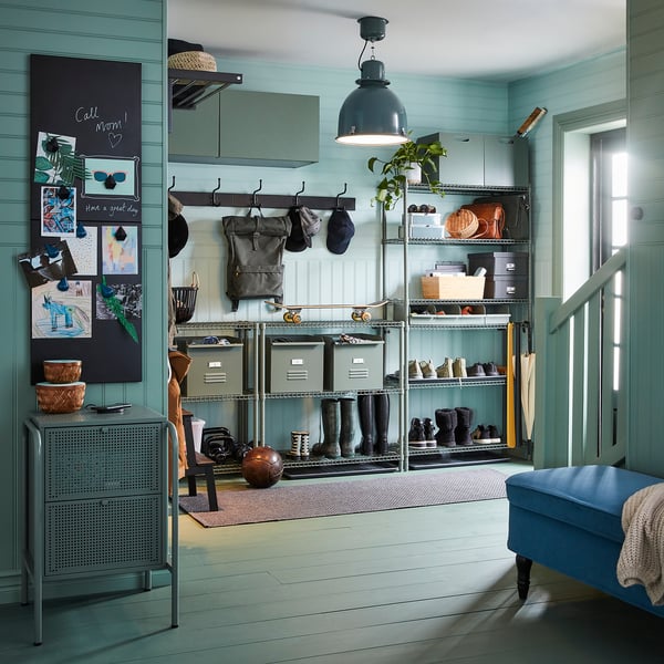Organised entryway with OMAR storage unit in green. Hooks, shelves with boots and boxes, and a bench with a blue cushion.