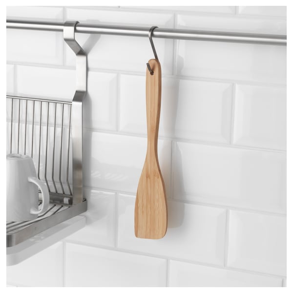 A bamboo spatula hangs from a hook near a dish rack, showcasing its convenient placement for easy access while cooking.
