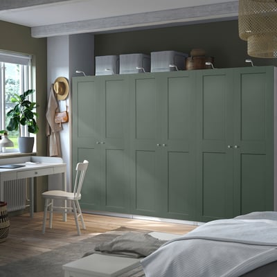 Modern bedroom tall teal PAX wardrobe, larger than nearby desk, with closed cabinets, hanging hat, basket, and white bed.