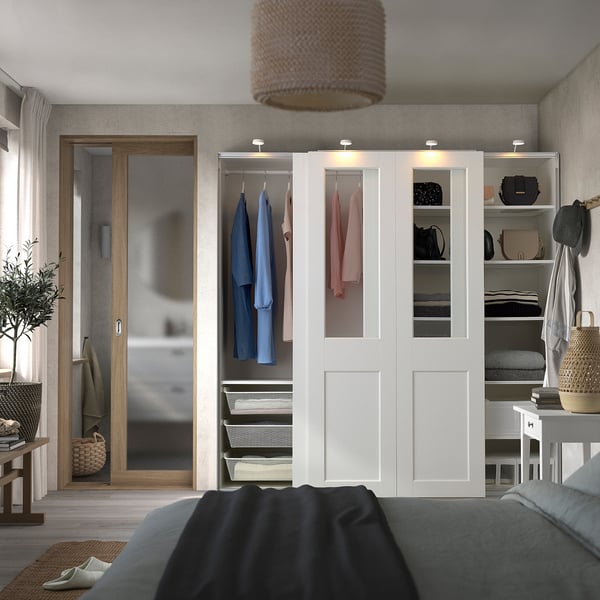 Modern bedroom with large PAX wardrobe, colourful clothes, and warm lamp.